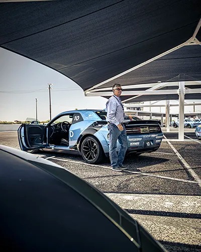 man smiling behind a car